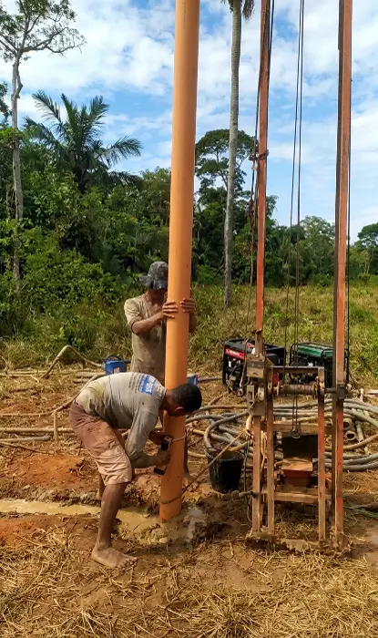 Equipe perfurando poço com sonda no meio do mato