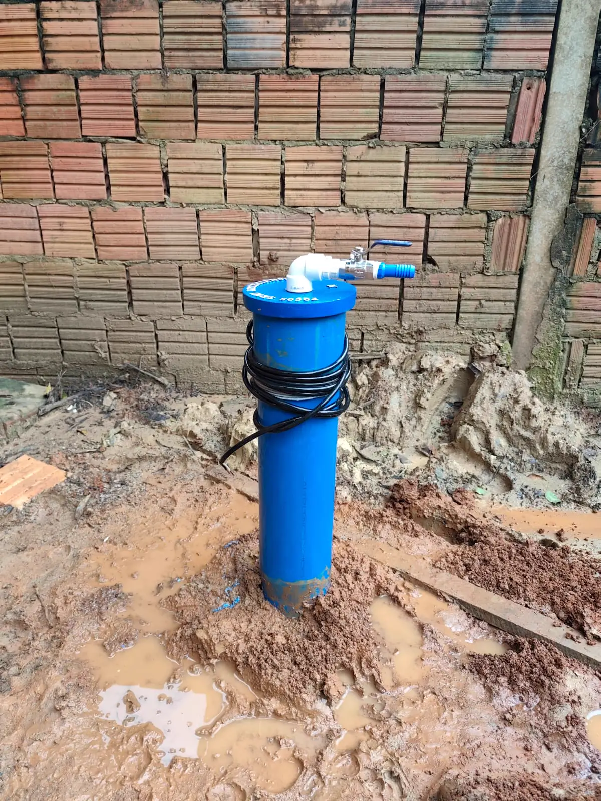 Poço instalado encostado em parede de tijolo, pronto pra bomba